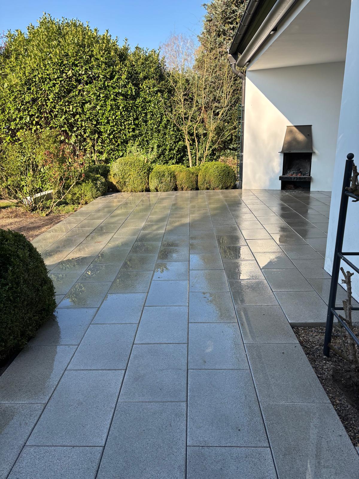 Frisch gepflasterte Terrasse aus grauen Natursteinplatten mit Außenkamin